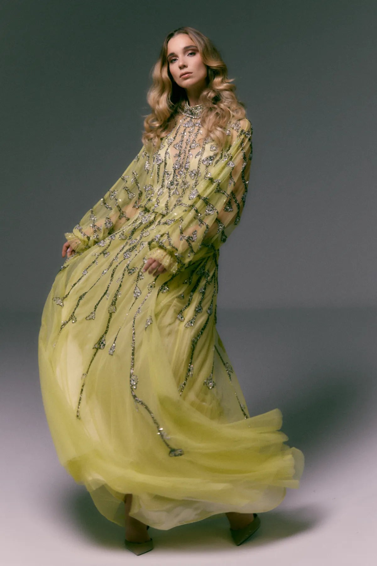 Woman wearing a long, elegant yellow dress with intricate detailing against a neutral background